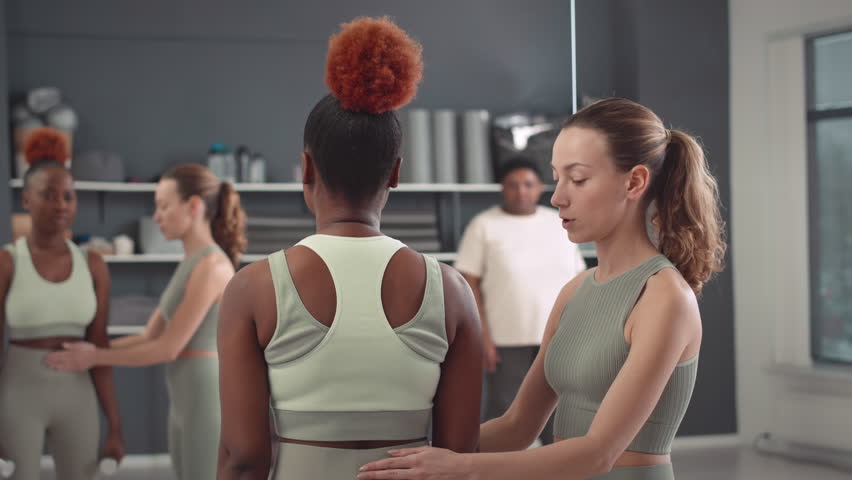 Young Caucasian female fitness coach showing Black woman how to do biceps curl with dumbbells standing in front of mirror during group class in studio Royalty-Free Stock Footage #1103651109