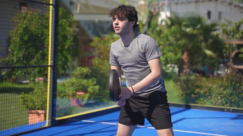 Front shot slow motion closeup of a young boy padel player practicing hitting the ball on the fly on a padel court outdoors in summer. Warm-up exercises.