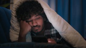 Sad sleepy guy Latino tired man upset Arabian sleeping napping boring Indian male at night evening dark home under blanket cover with duvet scrolling mobile phone addict smartphone bored social media - Powered by Shutterstock - Get 15% off with code: PIKWIZARD15