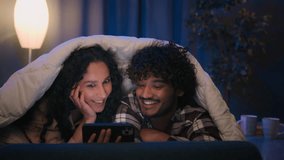 Multiracial couple man and woman at night home using mobile phone shocked amazed with online news shock wonder smartphone social media at evening on couch under blanket cover with duvet gadget addict - Powered by Shutterstock - Get 15% off with code: PIKWIZARD15