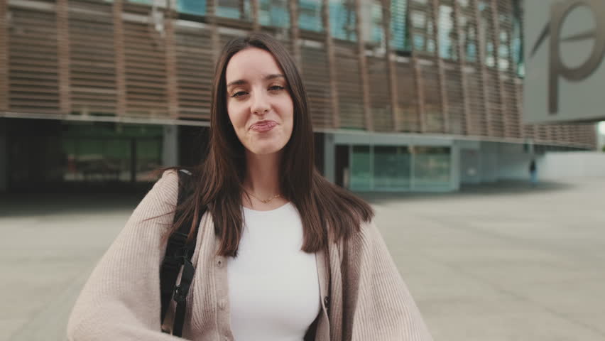 Girl student stands outside the university building crosses her arms, looks at the camera and smiles