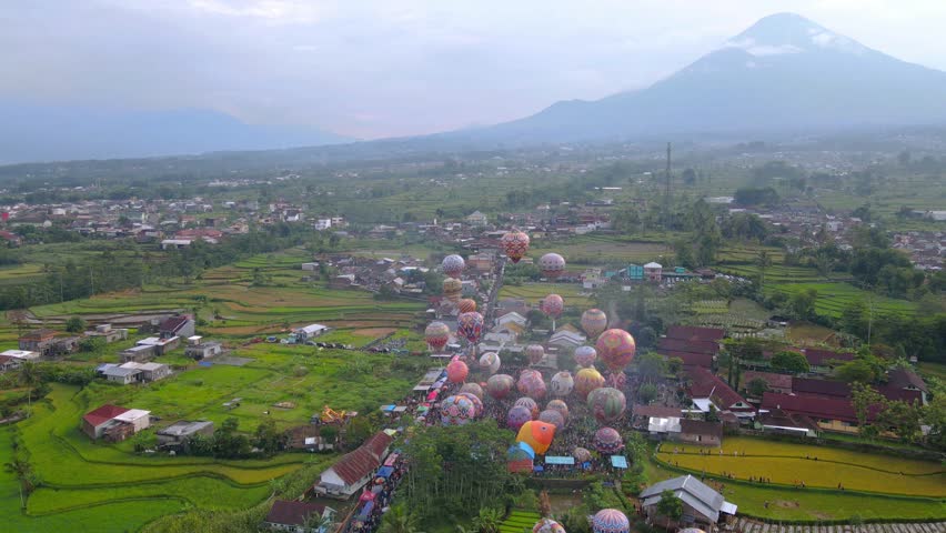 Aerial view of Colorful air balloon floating on the air with view of rural landscape and mountain on the background. Air balloon festival held in Indonesia like the one in Cappadocia. . 4K Aerial View