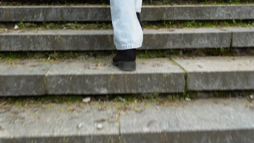 Woman legs in jeans walking on ancient stair back view. Female foot in black suede shoe go up step by step on old classic balustrade. Feet coming and climbing up. Disrupted stairway and stone railings