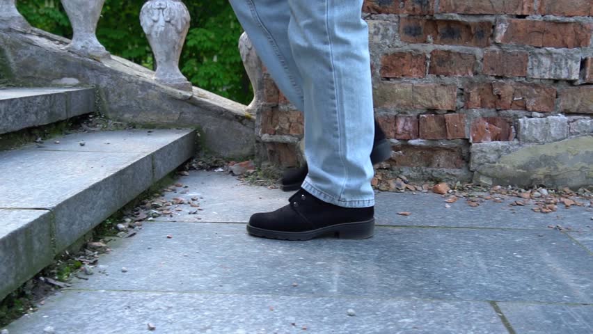Woman legs in jeans walking on ancient stair side view. Female foot in black suede shoe go up step by step on old classic balustrade. Feet coming and climbing up. Disrupted stairway and stone railings