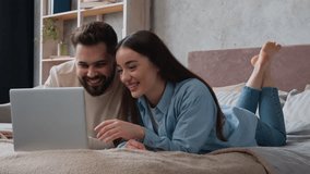 Happy Caucasian woman and man lying on bed carefree couple watch funny video on laptop in bedroom smiling husband boyfriend and wife girlfriend homeowners surfing computer website having fun joy laugh - Powered by Shutterstock - Get 15% off with code: PIKWIZARD15