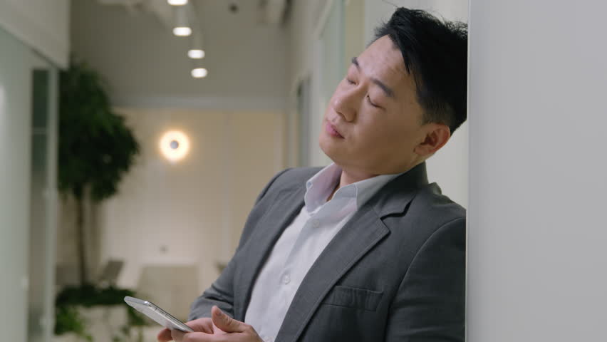 Tired upset Asian mature man exhausted 40s chinese businessman overworked mobile phone problem receive bad message weary male entrepreneur in office hallway feel despair overload cellphone app trouble | Shutterstock HD Video #1103679823