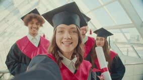 In Front of the Camera, Girl Graduate Made a Selfie Video Discussing Something After Graduation she Holds the Camera with One Hand in the College Hallway