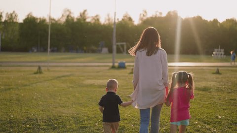 Mother with little children walk joining hands along field in park backside view slow motion. Cute family rests together. Public place for activity Video de stock