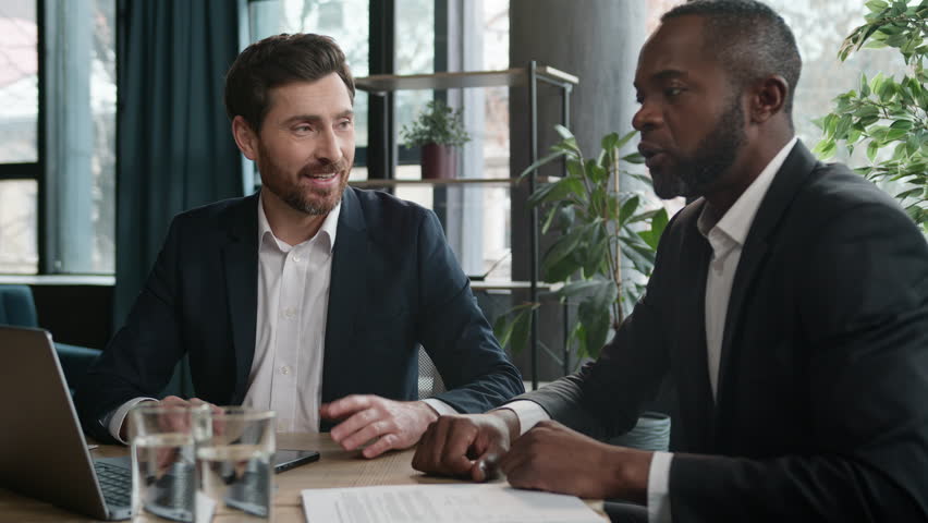 Diverse men colleagues business partners two multiracial businessmen emotional discuss project online startup laptop Caucasian man signing contract writing notes insurance investment sales in office Royalty-Free Stock Footage #1103695871