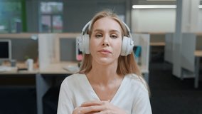 Portrait of a cheerful woman designer against the background of international office space, young woman in headphones communicates by video call, talks looking at the camera, template.
