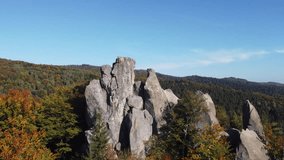 Flight over the rocks in autumn forest. Drone flies through the hole between rocks and over tree top. Tustan Carpathians Ukraine.