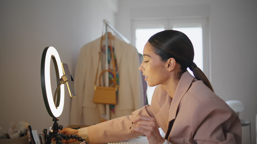 Beauty blogger changing light pushing buttons on stand at home studio closeup. Makeup artist looking cellphone screen choosing settings on lamp equipment. Happy woman using mobile phone on tripod