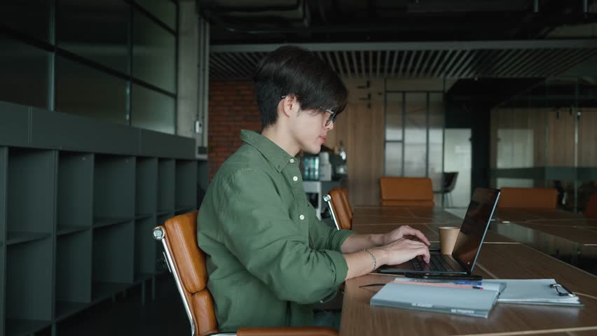 Confident Asian man in eyeglasses typing on mobile in a co-working room