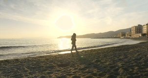 Silhouette of young woman walks at sunset along shore of Varazze waterfront beach in Liguria, Italy