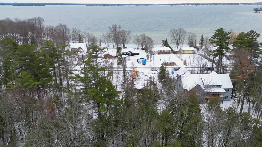 Drone flying towards lakeside houses on a snowy winter day.