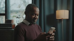 African American male employee focused on smartphone sitting in workplace at home. Footage of man enjoying conversation, checking messages on gadget. Online communication concept. Indoors - Powered by Shutterstock - Get 15% off with code: PIKWIZARD15