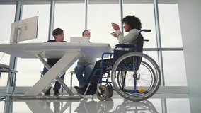 Disabled person at workplace in wheelchair. African american businesswoman sitting in wheelchair brainstorming at table with other colleagues. Teamwork in the office.People and business concept. - Powered by Shutterstock - Get 15% off with code: PIKWIZARD15