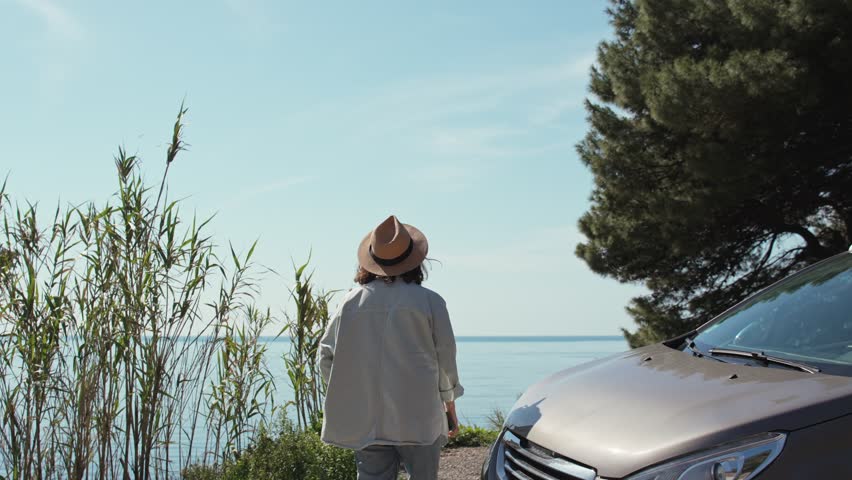 A young Caucasian woman enjoying the top view while standing next to the car during her solo trip to the sea.