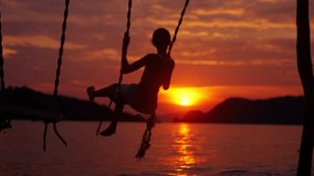 A video of a girl on the swing at a beach in Thailand during sunset