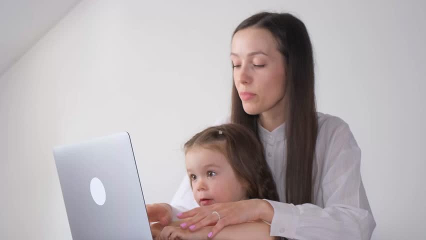 A young mother soothes her little daughter by letting her play on the laptop. Naughty children | Shutterstock HD Video #1103745565