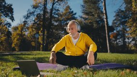 Focused man in his 60s meditating in urban park, watching online lesson, yoga
