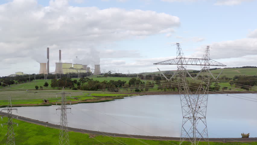 Slow orbit around high-voltage transmission lines from coal-fired power station in the distance. Loy Yang thermal power plant generates base-load electricity for Australians using fossil fuels.