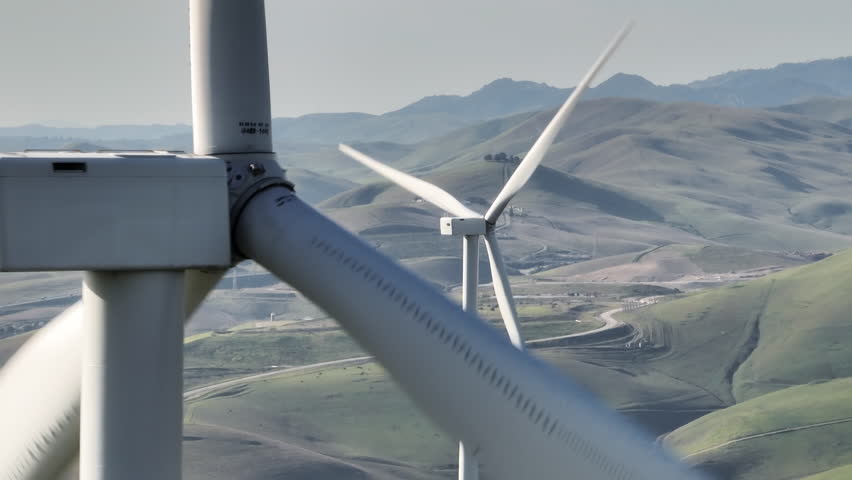 Windmill park green energy from drone view. Close up shot of windmill wind farm on green hills with rotating large windmill turbines generating renewable energy from wind. 4k footage California USA