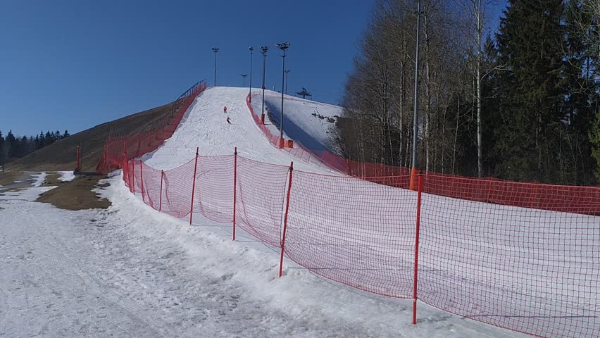 At the ski center, the slopes for safety are fenced with a mesh fence with plastic poles, behind which there are trees and stand lanterns. Snow melts in the spring sun and traces of skis and snowboard