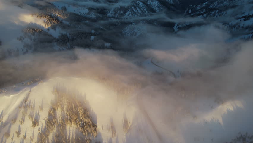 Aerial View of Winter Morning Fog and Mist Above Snow Capped HIlls and Pine Forest. Teton Montain Range, Wyoming USA