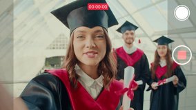 In Front of the Camera, Girl Graduate Made a Selfie Video Discussing Something After Graduation she Holds the Camera with One Hand in the College Hallway