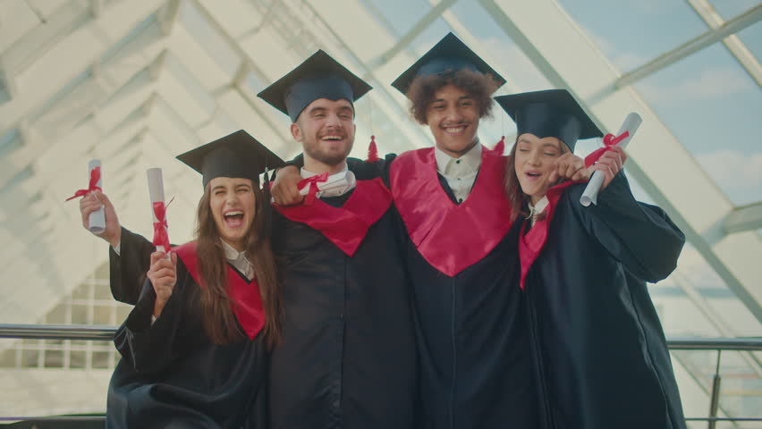 Portrait of Positive Group of four Graduates With Diplomas Hugging Together in Hallway of a University Building. Alumni of Educational institutions. Concept of Future Leaders