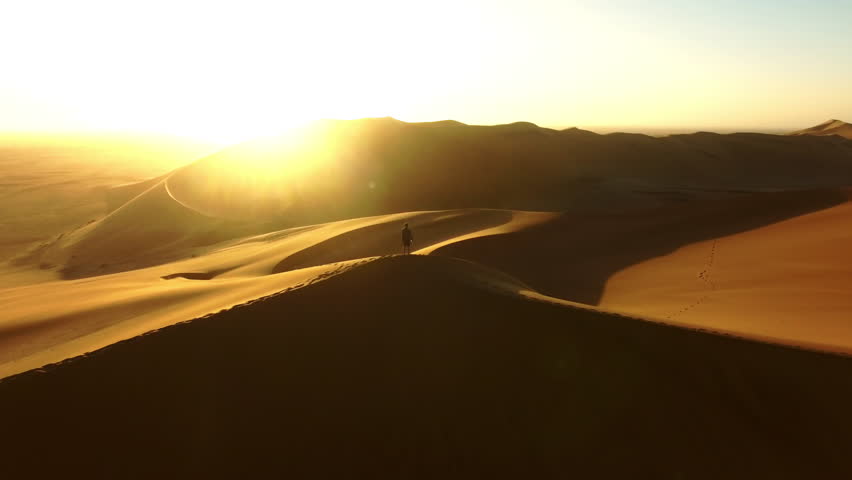 Travel, desert and silhouette of man at sunset with drone for destination, freedom or summer trip. Footprints, adventure and journey with guy on horizon of sand dunes on trip of Namibia vacation