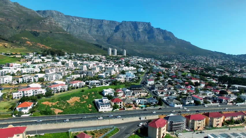 Architecture, buildings and house with drone of city in Cape Town for traffic, highway and urban road. Blue sky, mountains and travel or property with infrastructure, cityscape and cars in street Royalty-Free Stock Footage #1103760913
