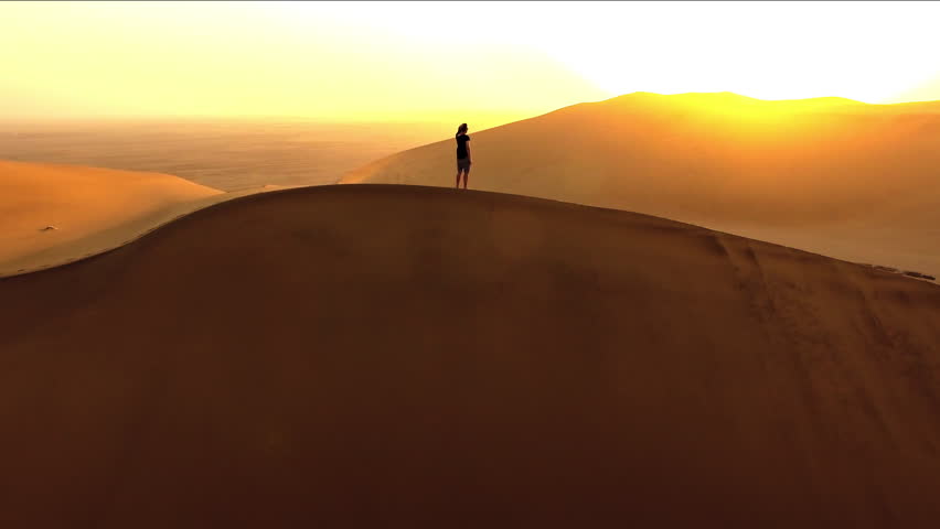 Sunset, drone and man walking in desert for hiking, adventure and freedom. Travel, discover and expedition hobby with person silhouette thinking on sand dunes hill for explorer, vacation and journey Royalty-Free Stock Footage #1103761205