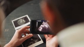 Happy future parents white woman and black husband enjoy baby moves ultrasound record via smartphone in living room extreme closeup slow motion