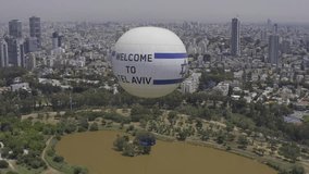 Aerial shot of a hot air balloon descending over Yarkon Park against the city sky - a park in Tel Aviv
