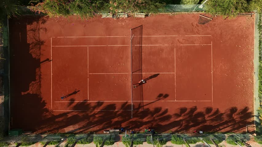 Tennis Clay Court Aerial Vertical Top View 4K top-down view of a young female sportsman during her practice. A close-up of a girl athlete serving the tennis ball. A young woman is hitting the b