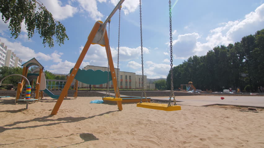 Orange plastic swing seat hangs on town sandy playground low angle shot. Attraction for children amusement in summer city dwelling district