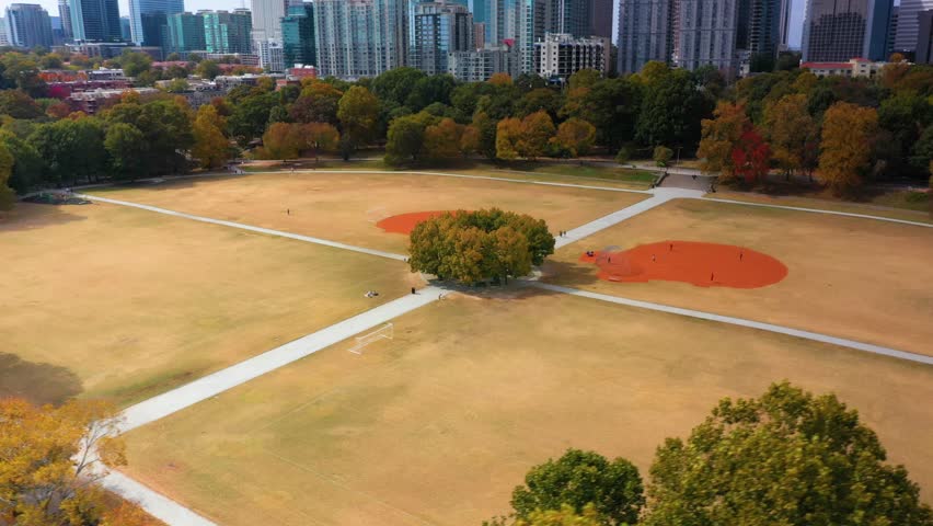 Aerial drone shot slowly flying around a patch of trees at the center of the softball fields at Piedmont Park in downtown Atlanta, Georgia.