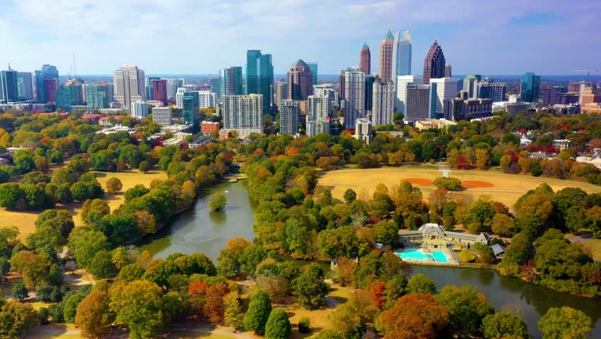 Aerial drone shot circling around Piedmont Park with downtown Atlanta, Georgia in the background. A lake, swimming pool, tennis courts, and softball fields are shown below. Royalty-Free Stock Footage #1103769827