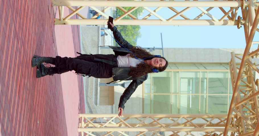 Young woman dancing while listening to music via headphones and online smartphone application. Slow motion vertical 4k video.
