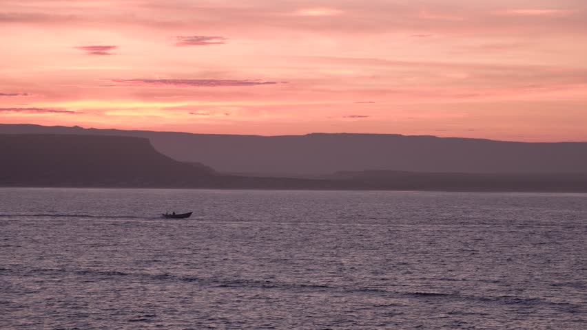 Small fishing boat passing fast from left to right during sunset in Baja California Mexico, Wide handheld shot