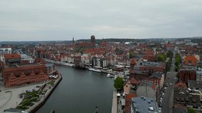 The drone video captures Gdansk's iconic St. Catherine's Church and the Basilica of St. Mary from above as it glides over a river. The stunning aerial view showcases the city's beauty.