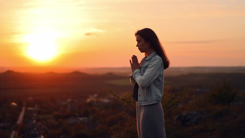 Girl folded hands in prayer silhouette at sunset. woman praying standing outdoors. A woman prays to God, asks for forgiveness of sins and peace in the world Royalty-Free Stock Footage #1103775471