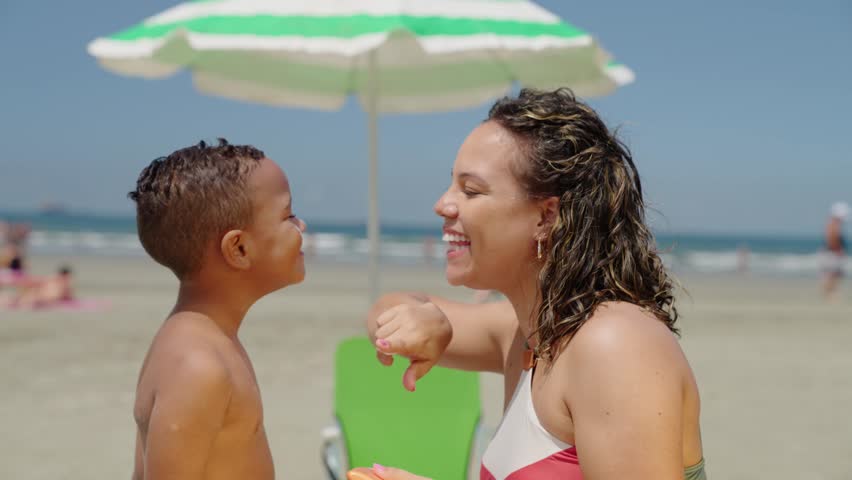 mother applying sunblock lotion on sons skin for sun protection little boy getting ready to swim on the beach with mom using sunscreen caring for childs health on sunny day 
 Royalty-Free Stock Footage #1103775671
