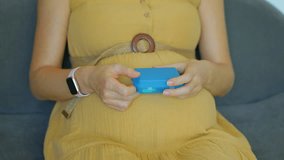 In this slow-motion video, a pregnant woman is seen sitting on a couch. She takes a pill of vitamins or food supplements from a plastic box with sections. The camera is focused on her hands and the