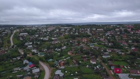 View of the landscape with cloudy weather taken from a helicopter. Clip. Gray sky over a small village with small residential buildings and a river.