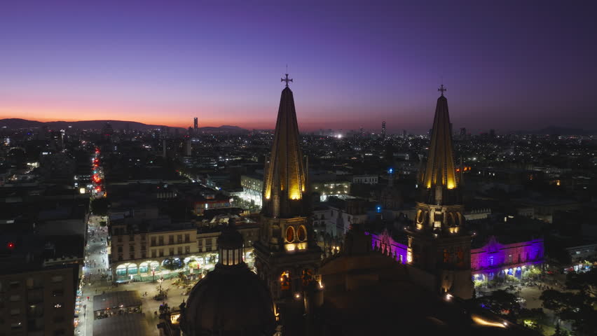 Cinematic pink purple sunset sky above Guadalajara Cathedral with night city on motion background in Mexico. Drone of historic architecture Cathedral with scenic night illumination. Aerial Guadalajara