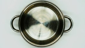 Water is poured into an iron pan on a white background. Isolated. The cook pours clean water into a chrome saucepan for boiling and cooking. Kitchenware. Beautiful video of clear water on the kitchen