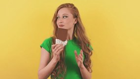 The young woman looks around and starts eating a bar of chocolate. A beautiful lady with red hair stands in front of the camera and enjoys the taste of milk chocolate.